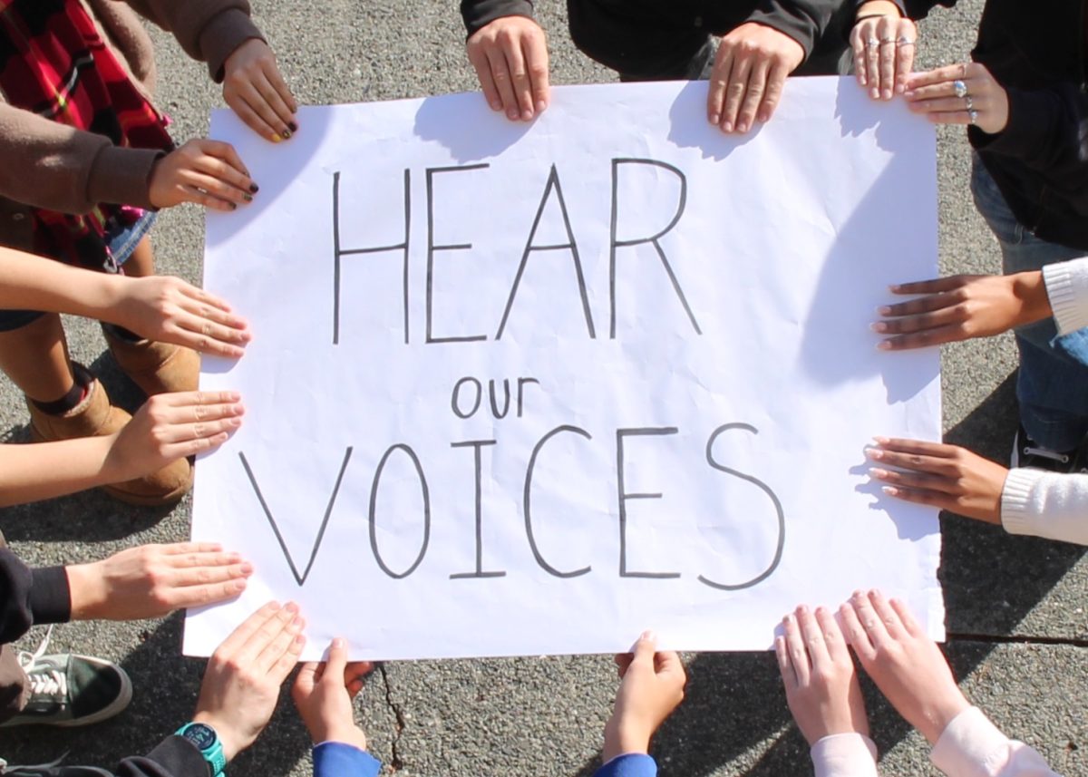 Students holding sign that says, "Here our voices."