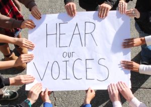 Students holding sign that says, "Here our voices."